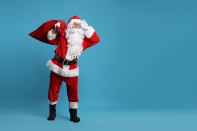 Photo of Santa Claus with bag of Christmas gifts posing on light blue background, space for text