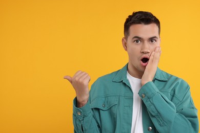 Photo of Special promotion. Emotional man pointing at something on orange background, space for text