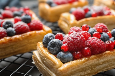 Photo of Cooling rack and fresh delicious puff pastry with sweet berries on grey table, closeup