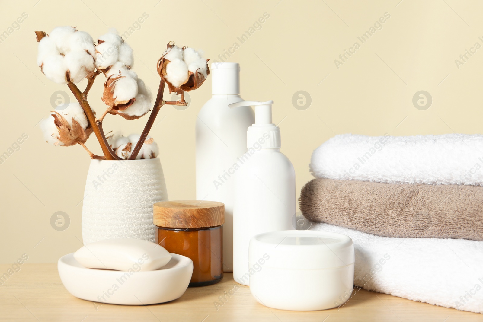 Photo of Different bath accessories and cotton flower on wooden table against beige background