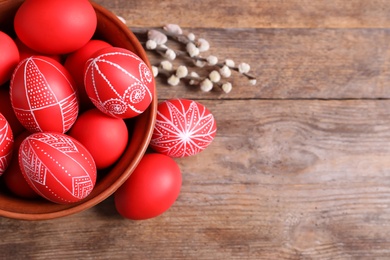 Photo of Bowl with red painted Easter eggs on wooden background, top view. Space for text