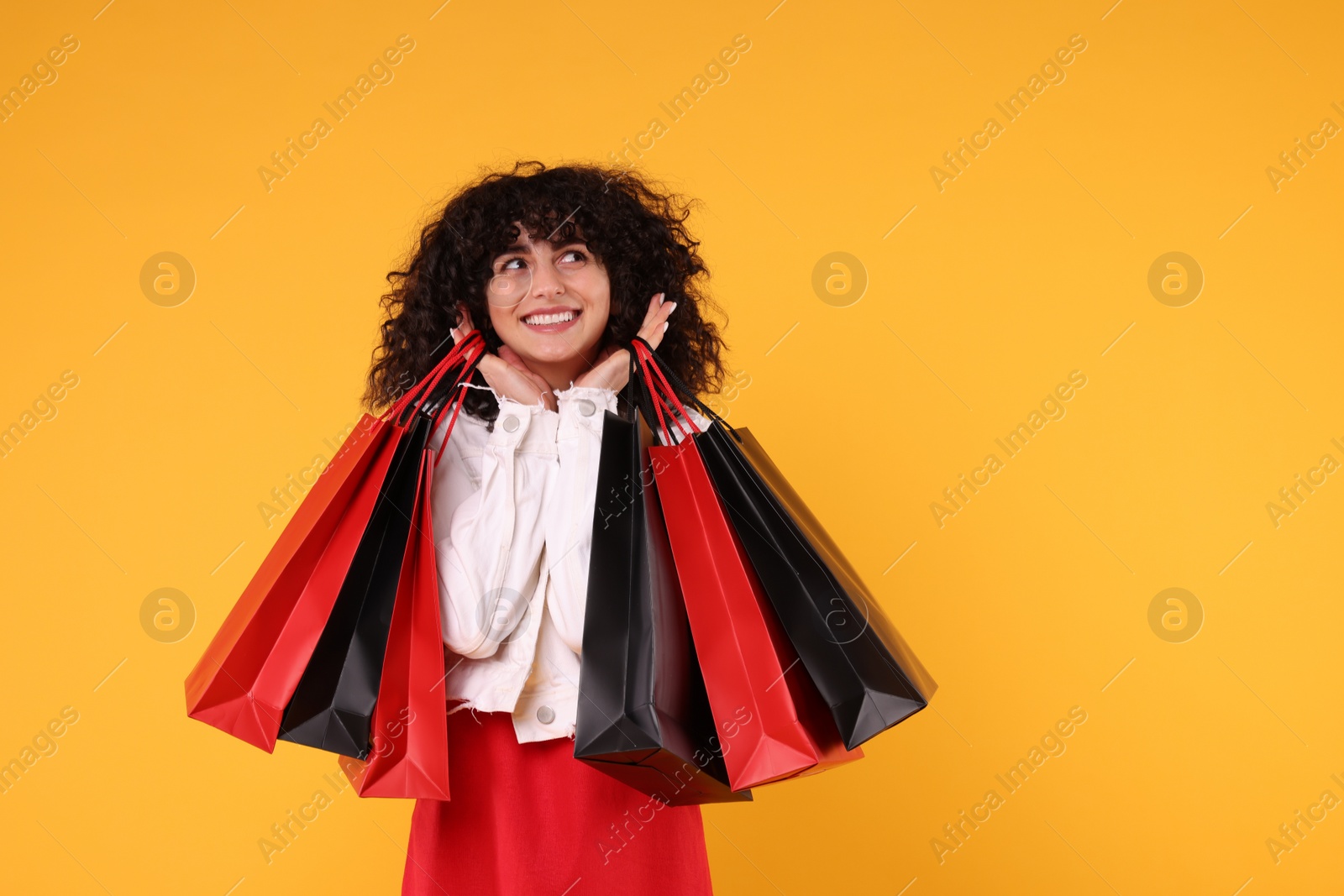 Photo of Happy young woman with shopping bags on yellow background. Space for text