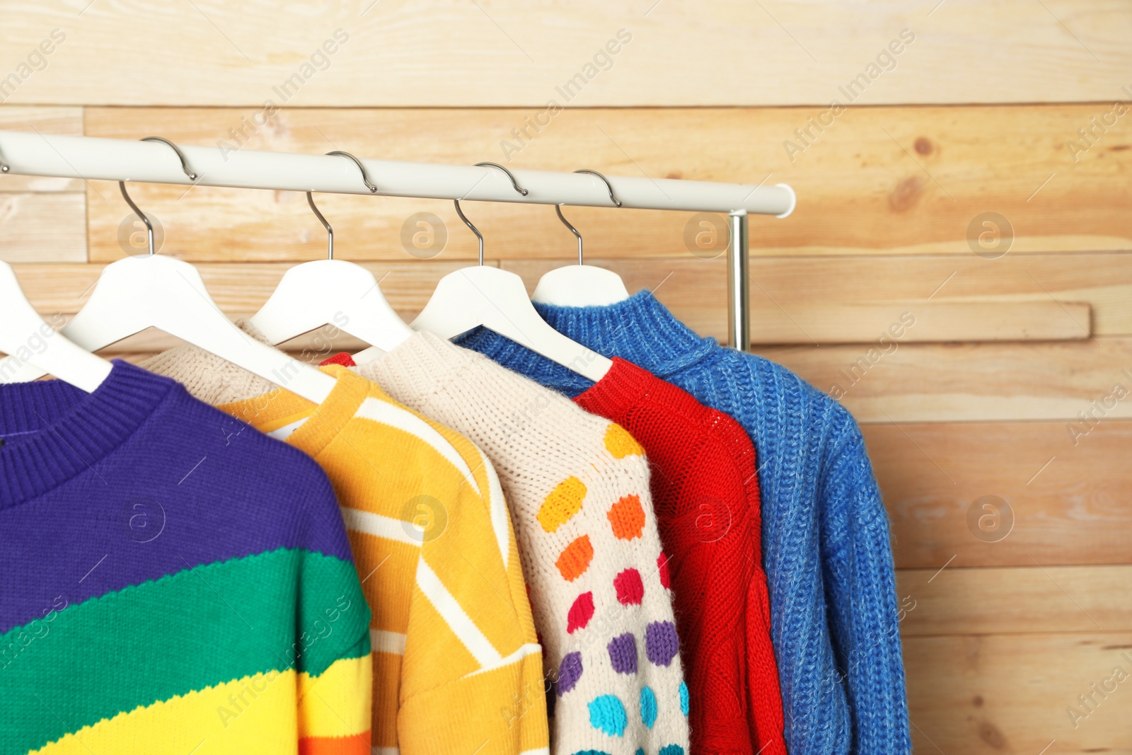 Photo of Collection of warm sweaters hanging on rack against wooden background