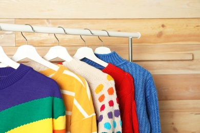 Collection of warm sweaters hanging on rack against wooden background