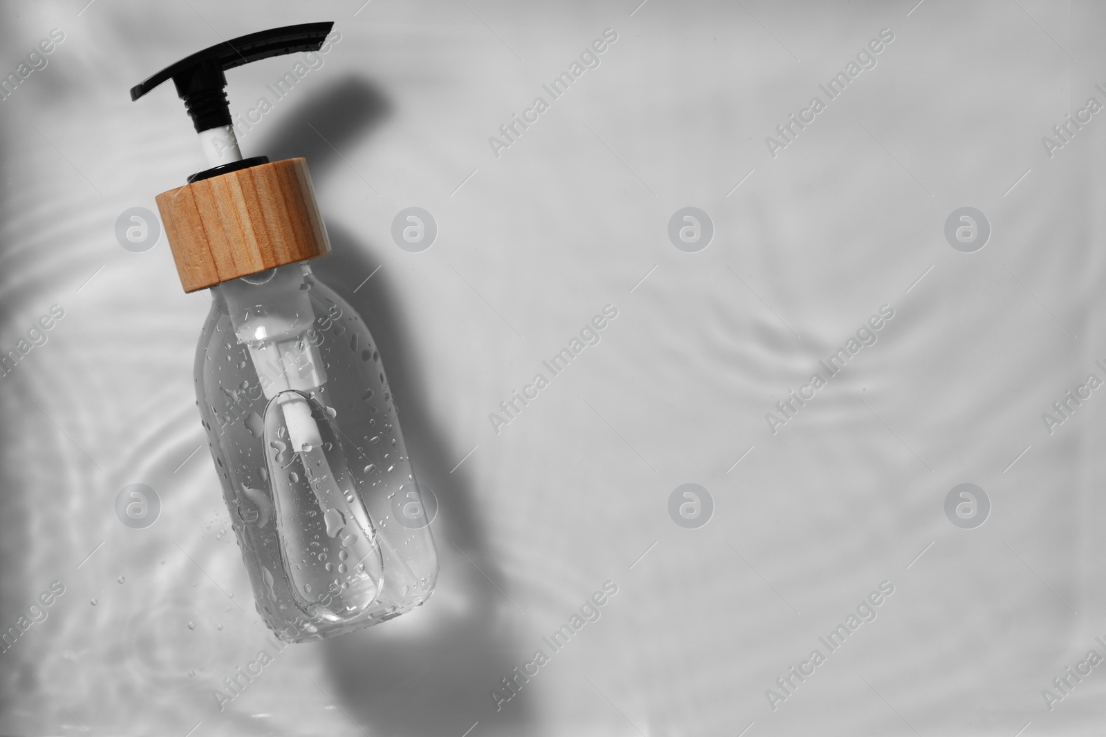 Photo of Bottle of cosmetic product in water on white background, top view. Space for text