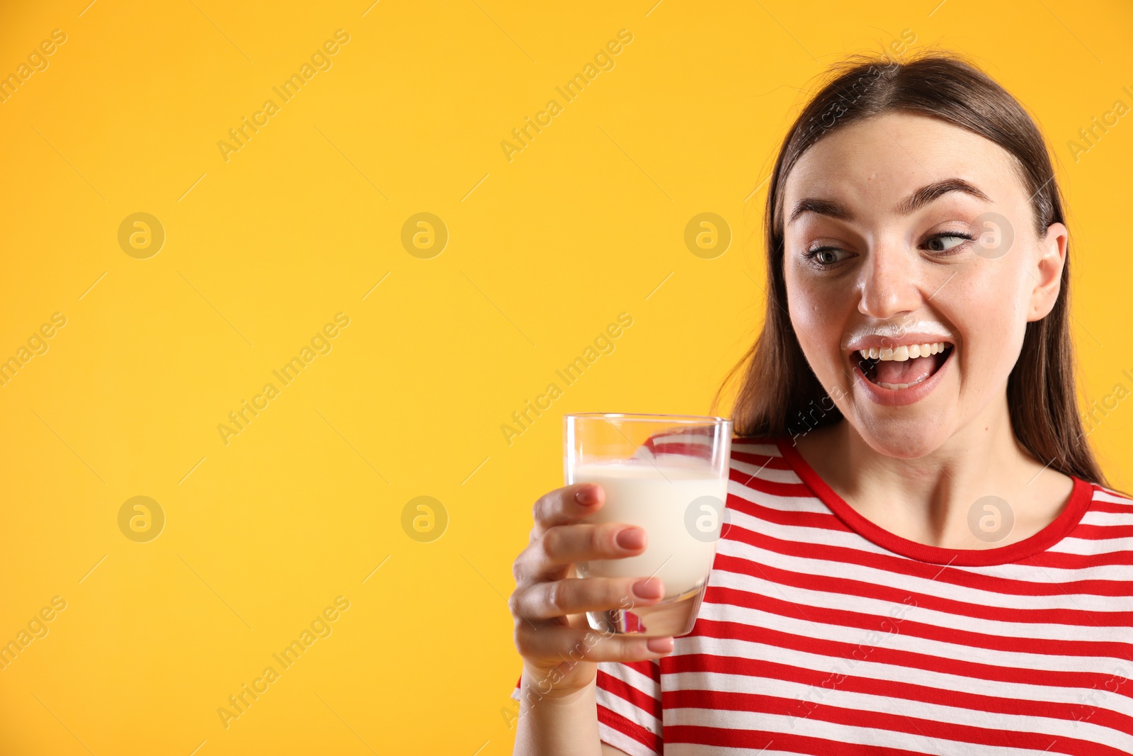 Photo of Emotional woman with milk mustache holding glass of tasty dairy drink on orange background, space for text