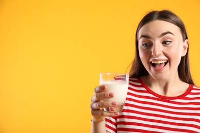 Emotional woman with milk mustache holding glass of tasty dairy drink on orange background, space for text