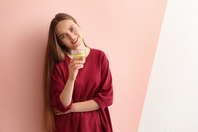Photo of Young woman holding glass of lemon water on color background