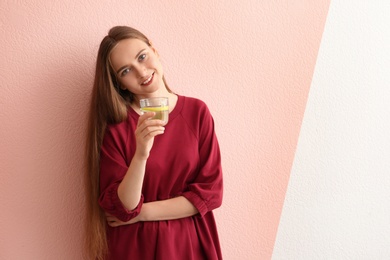 Young woman holding glass of lemon water on color background