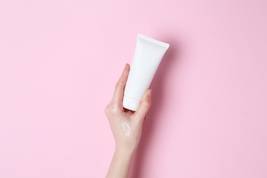 Photo of Woman holding tube of cream on pink background, closeup