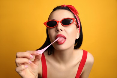 Photo of Fashionable young woman in pin up outfit chewing bubblegum on yellow background