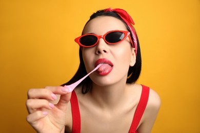 Fashionable young woman in pin up outfit chewing bubblegum on yellow background