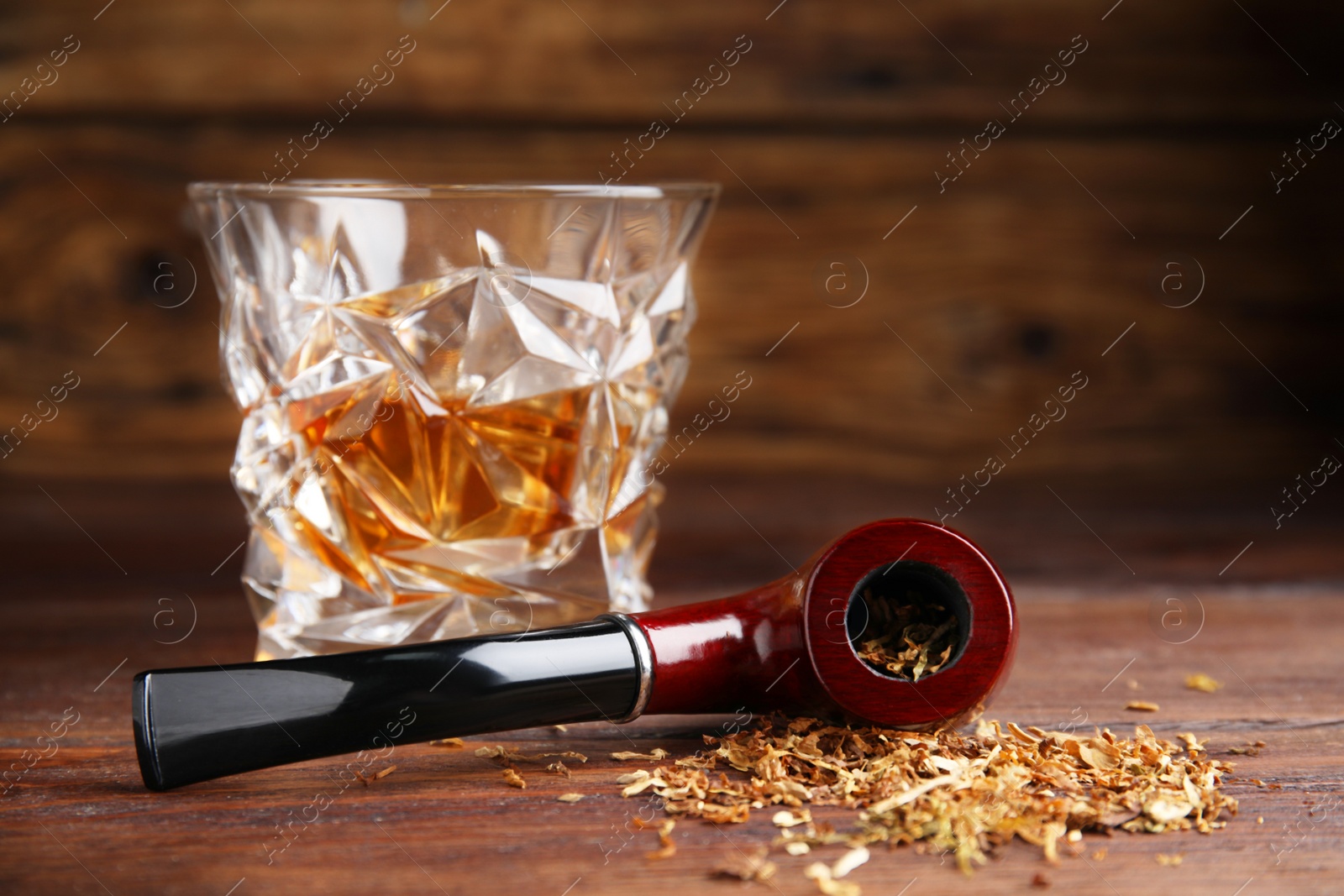 Photo of Smoking pipe with tobacco and glass of whiskey on wooden table