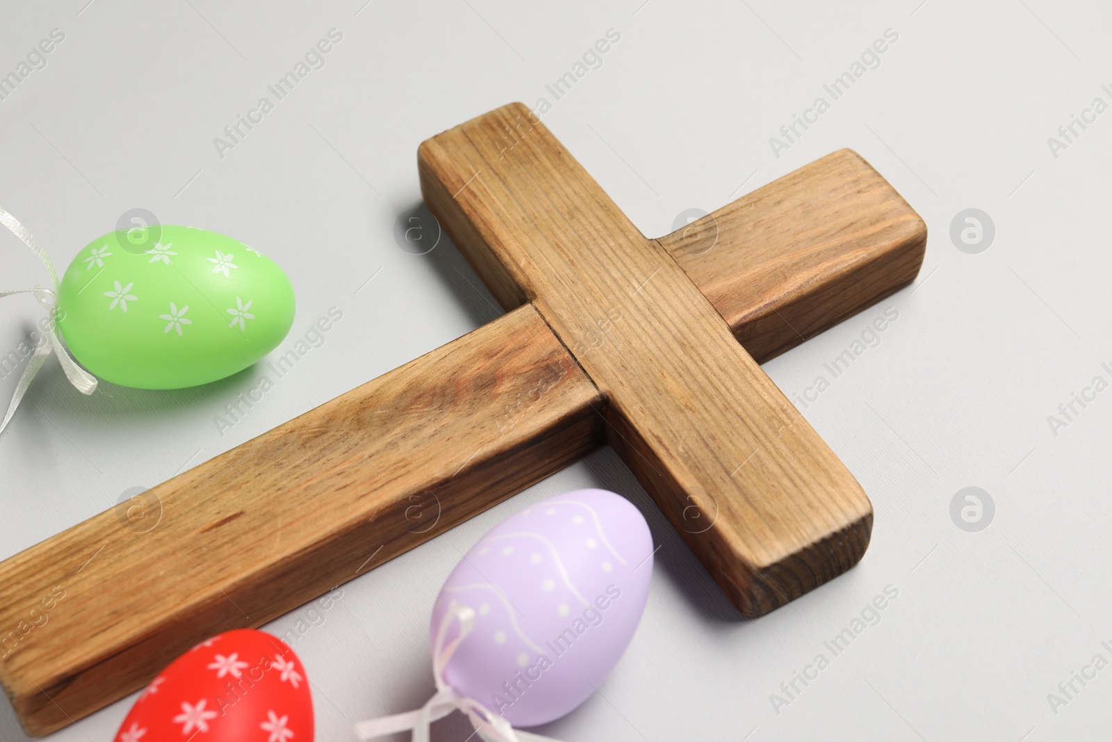 Photo of Wooden cross and painted Easter eggs on light grey background