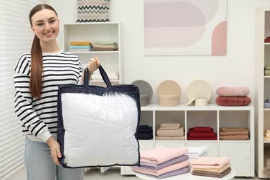 Photo of Smiling young woman holding bag with duvet in home textiles store. Space for text