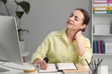 Young woman suffering from neck pain while working at table in office