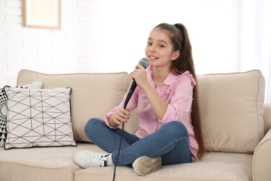 Photo of Cute girl with microphone on sofa in living room