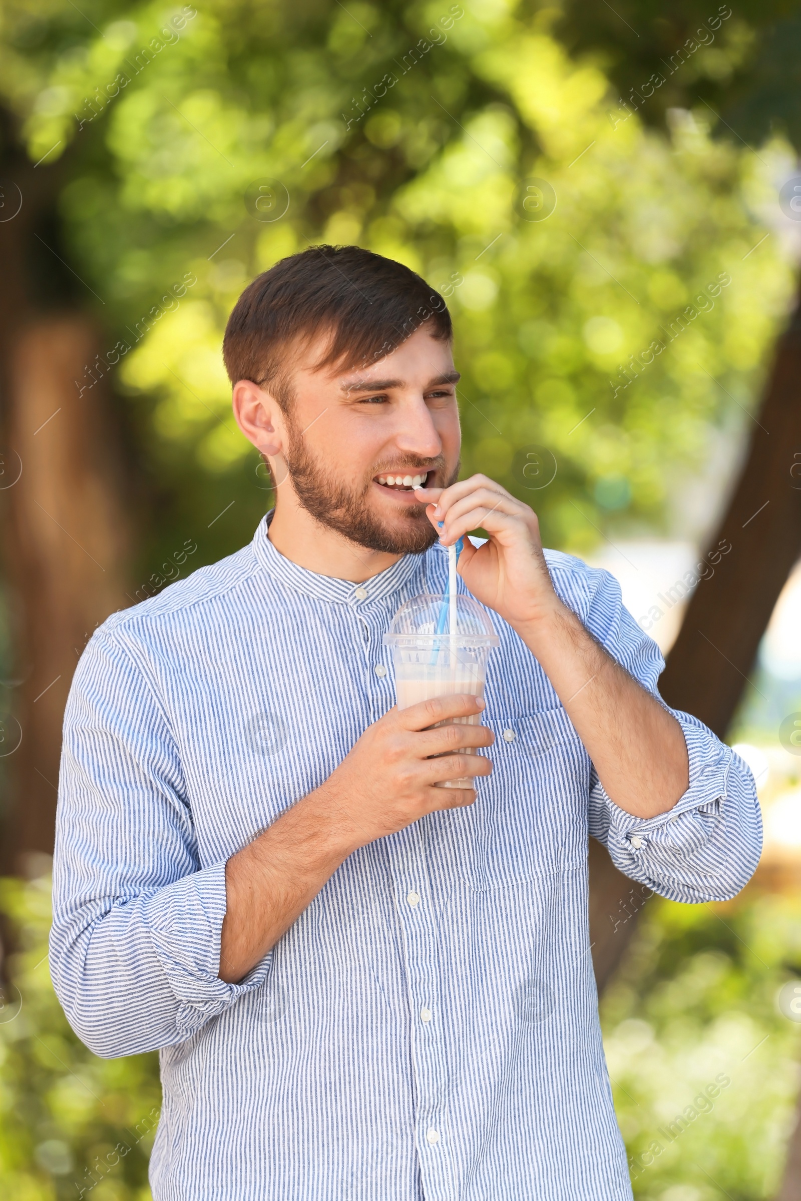 Photo of Young man with cup of delicious milk shake outdoors