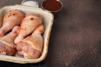 Photo of Fresh marinade and raw chicken drumsticks on brown table, closeup. Space for text