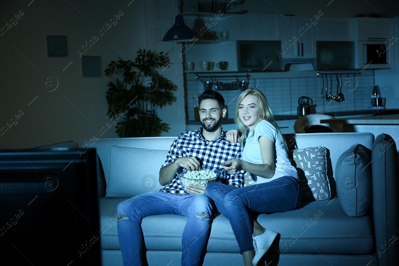 Photo of Young couple with bowl of popcorn watching TV on sofa at night