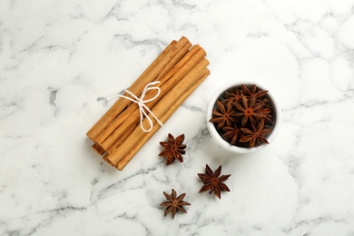 Aromatic cinnamon sticks and anise on white marble table, flat lay