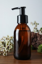 Photo of Bottle of hydrophilic oil and beautiful flowers on wooden table
