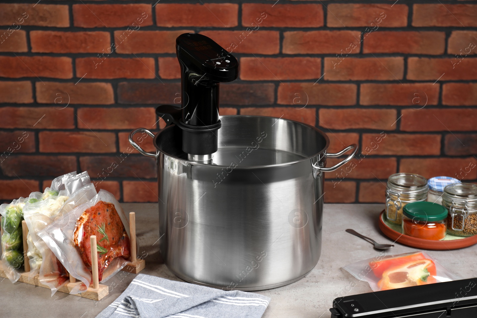 Photo of Thermal immersion circulator in pot and ingredients on beige table. Vacuum packing for sous vide cooking