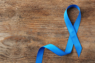 Photo of Blue awareness ribbon on wooden background, top view with space for text. Symbol of social and medical issues