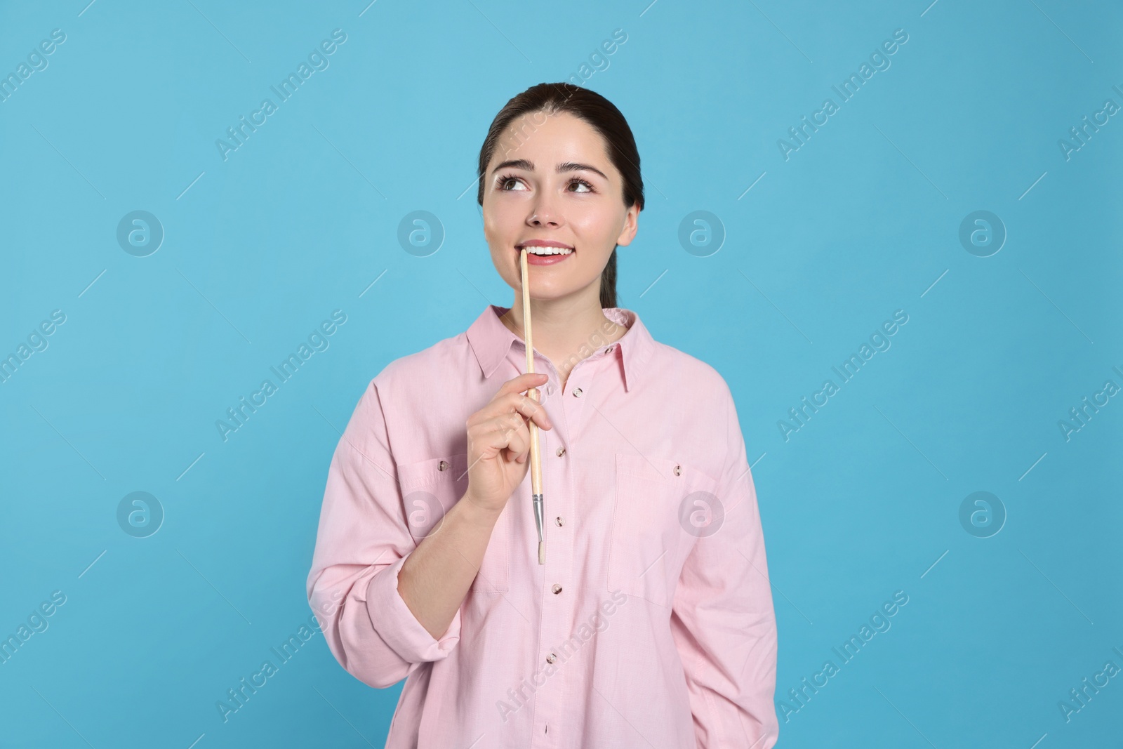 Photo of Woman with paintbrush on light blue background. Young artist