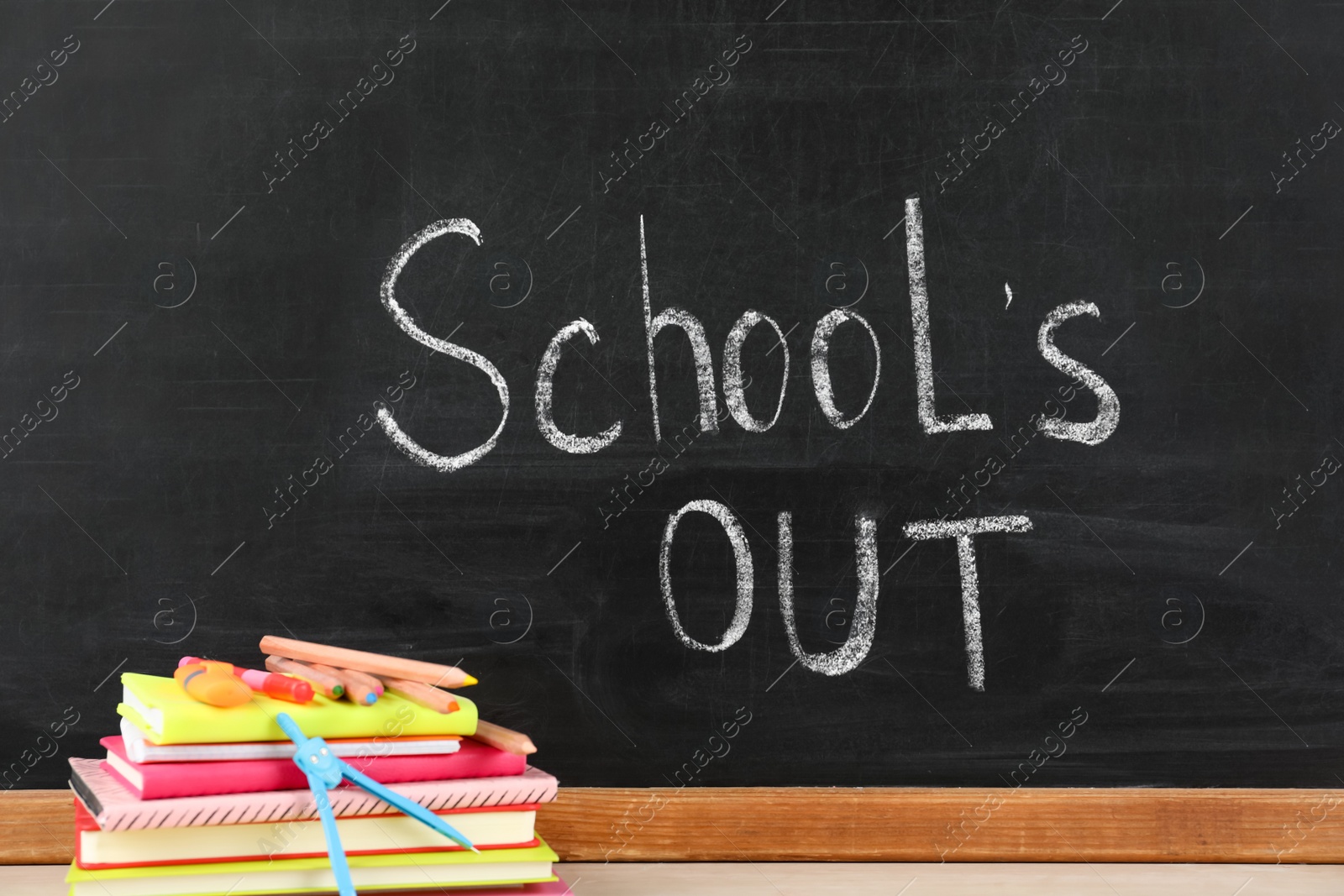 Photo of Stationery on table near blackboard with text School's Out. Summer holidays