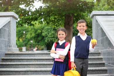 Cute children with apple, stationery and backpacks near stairs in park