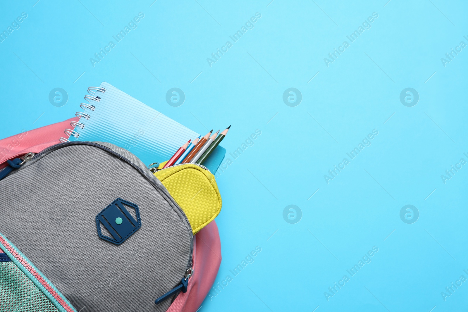 Photo of Stylish backpack with different school supplies on light blue background, top view. Space for text