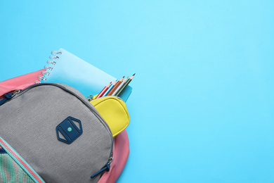 Photo of Stylish backpack with different school supplies on light blue background, top view. Space for text