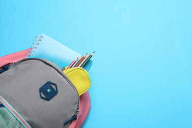 Stylish backpack with different school supplies on light blue background, top view. Space for text