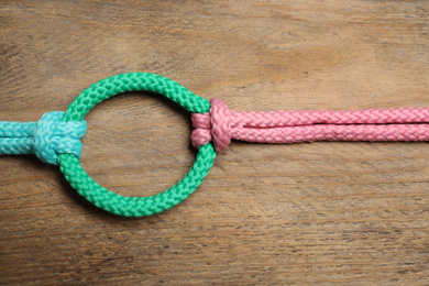 Photo of Colorful ropes tied together on wooden background, top view. Unity concept