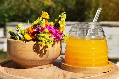 Delicious fresh honey and beautiful flowers on wooden board in apiary