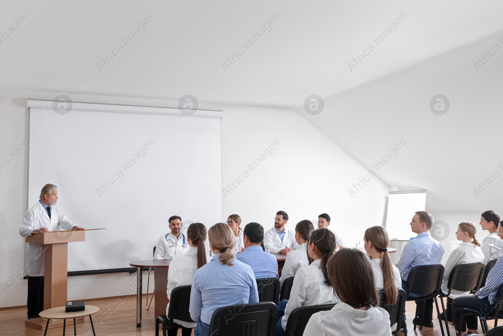 Photo of Senior doctor giving lecture in conference room with projection screen