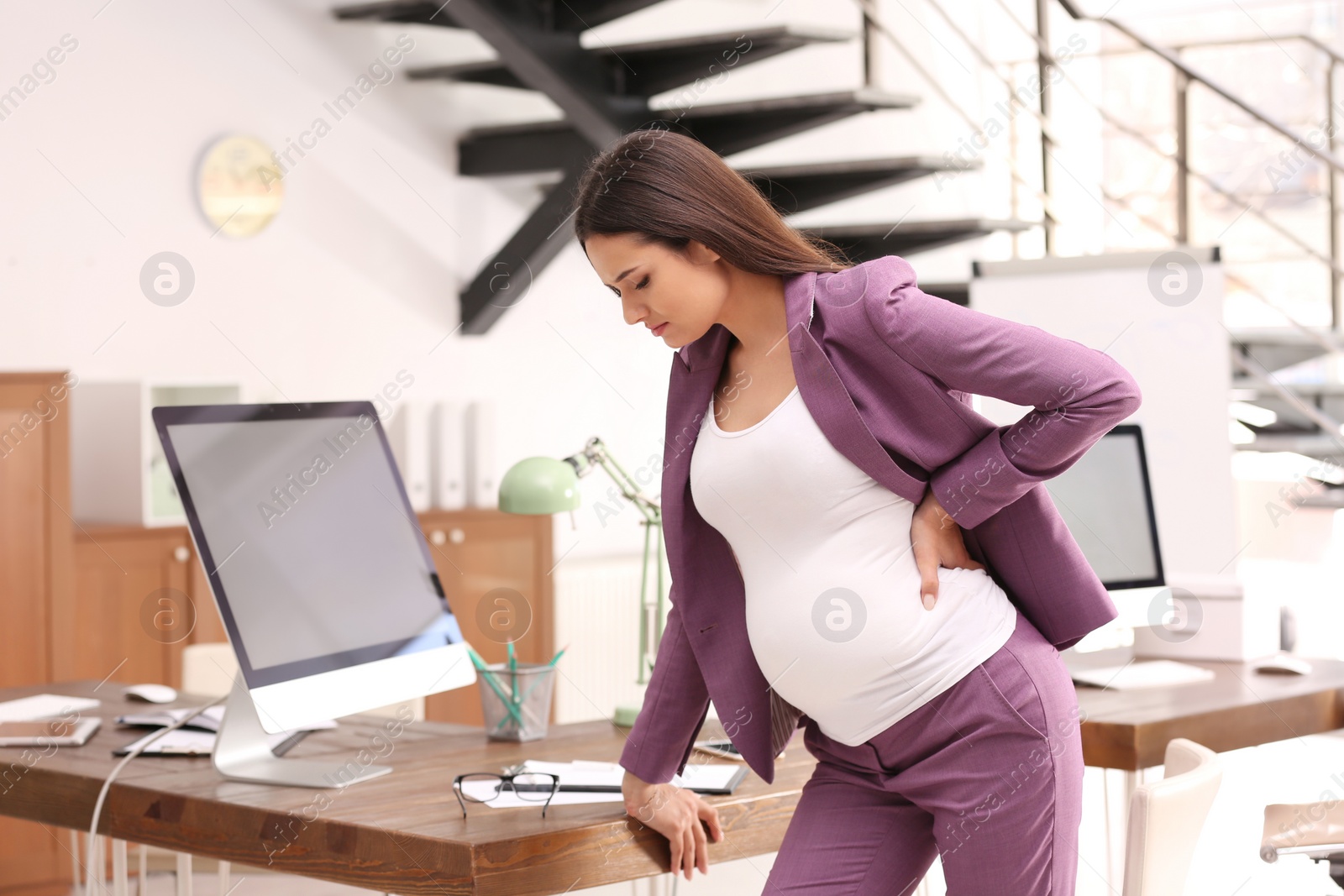 Photo of Young pregnant woman suffering from pain while working in office