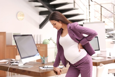 Photo of Young pregnant woman suffering from pain while working in office