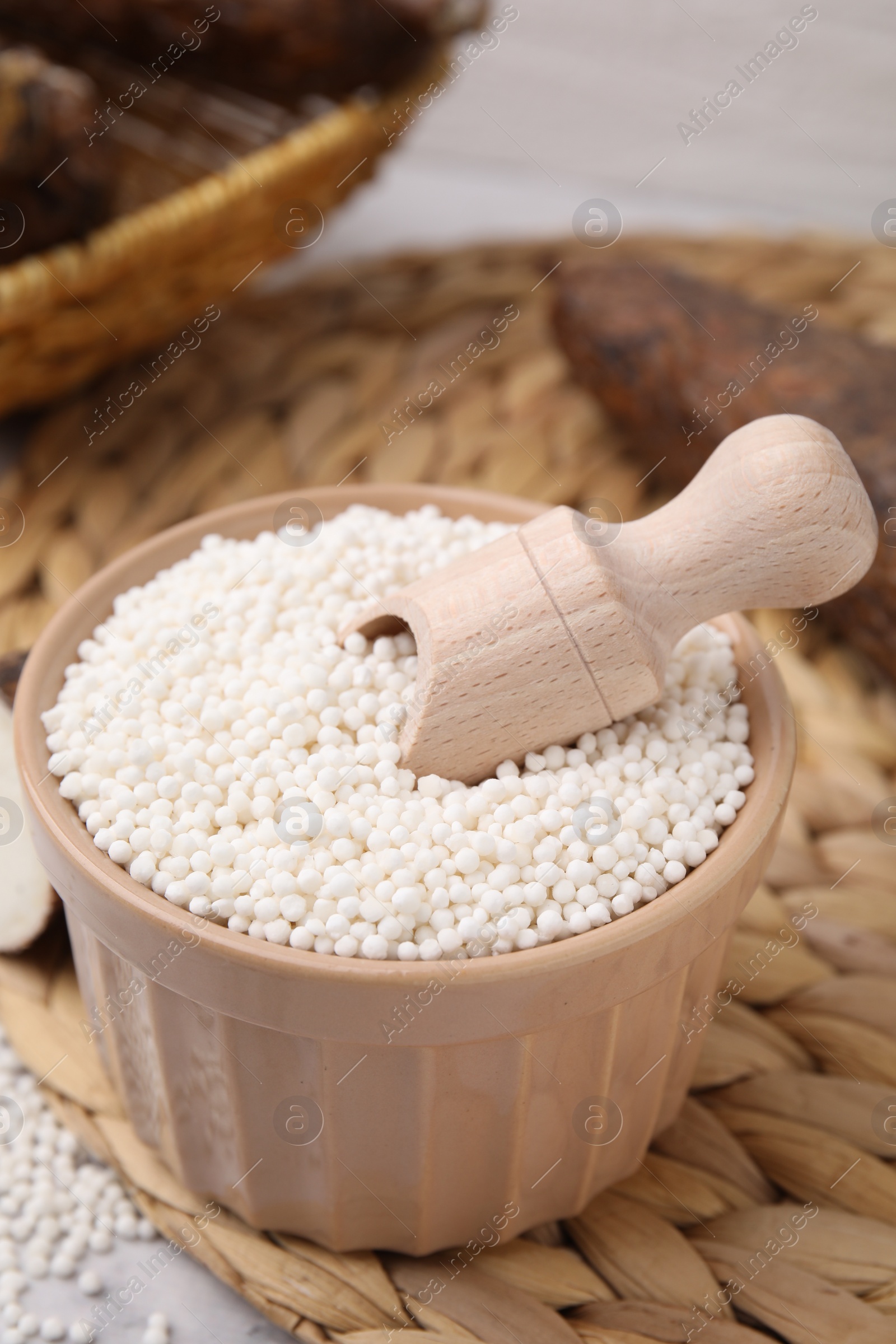 Photo of Tapioca pearls in bowl and cassava roots on white table, closeup