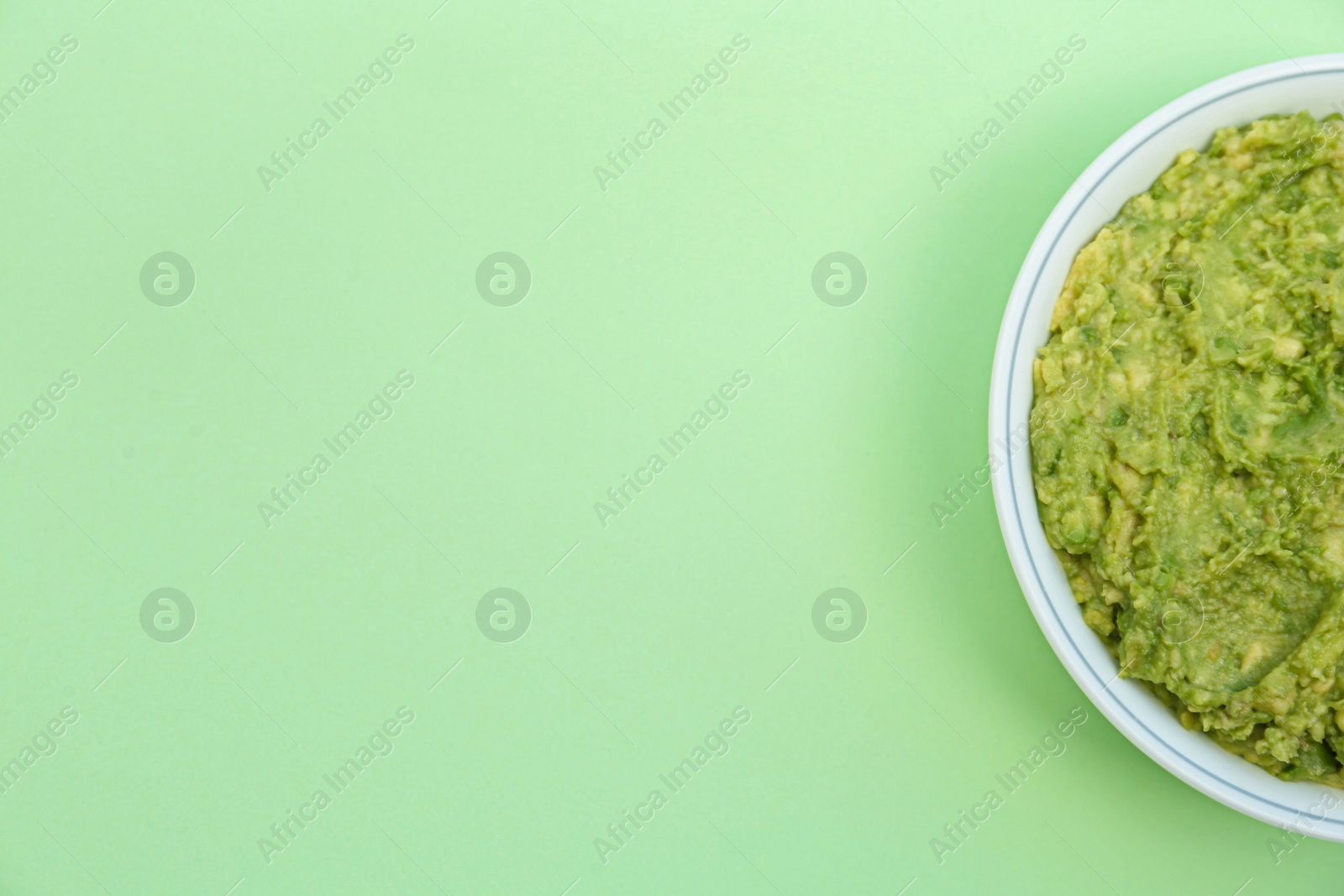 Photo of Delicious guacamole made of avocados on light green background, top view. Space for text