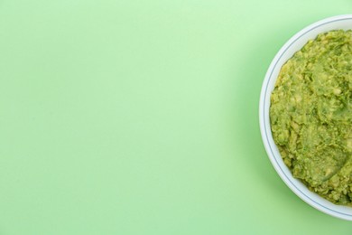 Delicious guacamole made of avocados on light green background, top view. Space for text