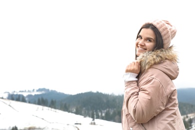 Photo of Young woman in warm clothes near snowy hill, space for text. Winter vacation