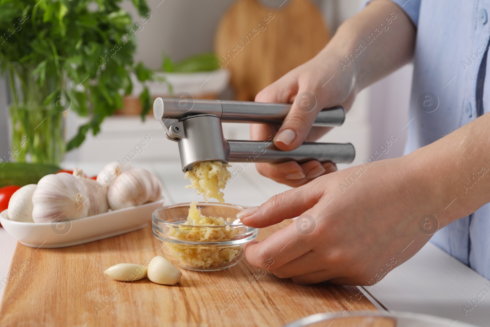 Photo of Woman squeezing garlic with press at white table in kitchen, closeup