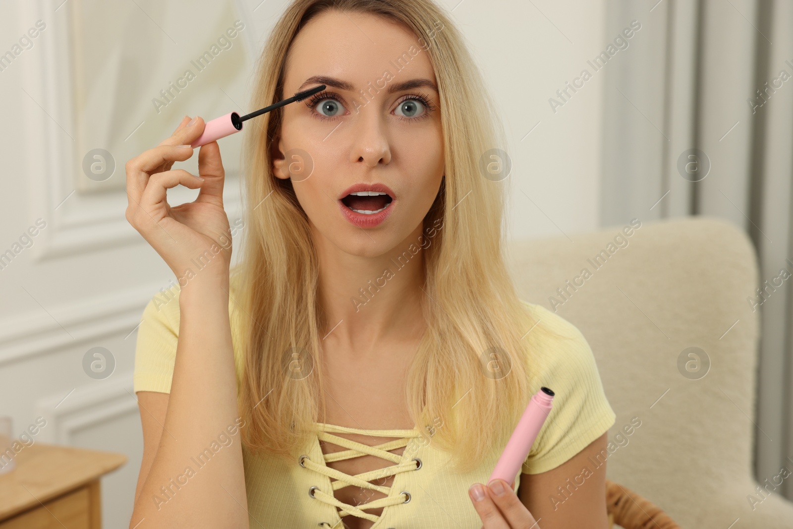 Photo of Beautiful emotional woman applying mascara at home