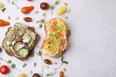 Tasty vegan sandwiches with vegetables and microgreens on light grey table, flat lay. Space for text