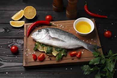 Composition with fresh raw dorado fish and spices on black wooden table