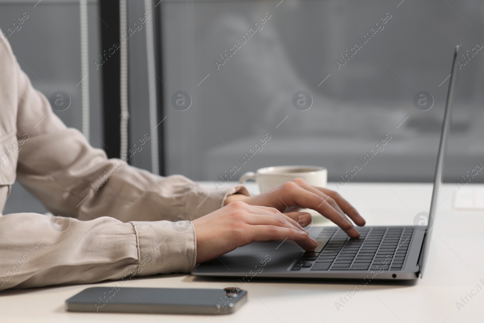 Photo of Woman working with laptop at white desk in office, closeup