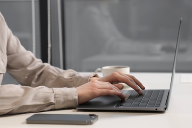 Woman working with laptop at white desk in office, closeup