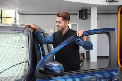Young man near new car in dealership